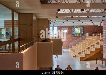 Moderne Inneneinrichtung einer Bildungseinrichtung mit einer großen, holzernen, amphitheaterartigen Treppe und weißen Metallgeländern auf der rechten Seite. Stockfoto