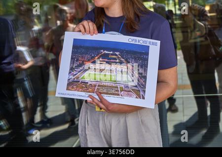 Eine Frau, die ein marineblaues T-Shirt und hellfarbene Hose trägt, hält während eines Tag der offenen Tür ein großes Plakat mit einer architektonischen Darstellung Stockfoto