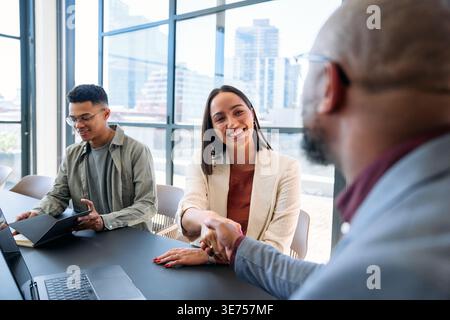 Lächelnde junge Geschäftsfrau schüttelt tagsüber im Konferenzraum im Büro die Hand mit einem Kollegen Stockfoto