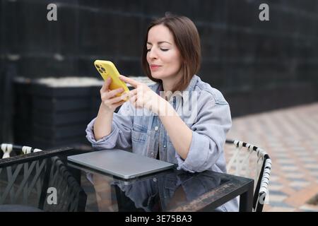 Junge Frau mit Smartphone im Freien. Porträt einer kaukasierin mit Telefon auf der Terrasse des Cafés. Stockfoto