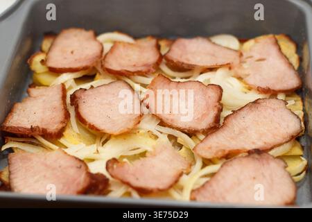 Eine Nahaufnahme eines Gerichts mit Räucherfleisch auf einem Bett aus Zwiebeln und Kartoffeln. Das Essen ist ordentlich in einem Backblech angeordnet Stockfoto