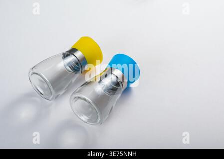 Zwei Gewürzmühlen, klares Glas und bunte Kunststoffdeckel, Akzente aus Edelstahl. Studio-Aufnahme auf sauberer weißer Oberfläche. Konzentrieren Sie sich auf minimalistisches Design, Küche Stockfoto