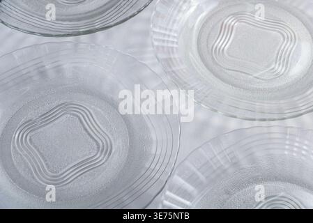 Mehrere klare dekorative Glasplatten auf dezent weißem, strukturiertem Stoff. Fokus auf leichtes Spiel, Materialtransparenz. Kommerzielle Potenziale für den Küchenkrieg Stockfoto