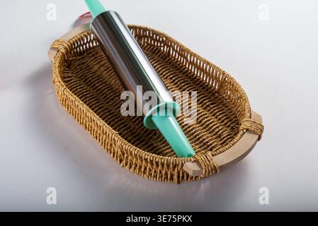 Rollstift mit blauen Griffen im Korb isoliert auf weiß. Die weiche Studiobeleuchtung sorgt für eine angenehme Textur. Neutrale Farbpalette. Backkonzept für f Stockfoto