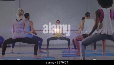 Leitender Trainer im gelben Tank, dunkle Leggings, die den Kurs in der breiten Hocke auf blauen Matten führt, Barre Stockfoto