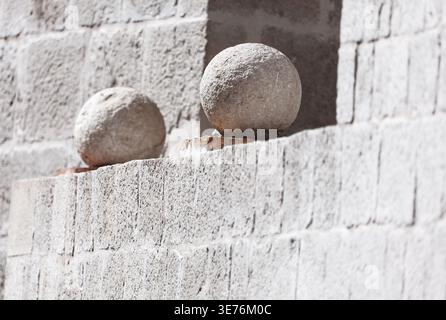 Zwei runde Steinkugeln ruhen auf einer Stufenmauer aus hellgrauen Blöcken. Die Oberflächenstruktur der Wand und der Kugeln erscheint rau und witterungsbedingt Stockfoto