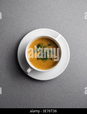 Warme Suppe in weißer Tasse, garniert mit frischen Kräutern. Einfache, elegante Präsentation auf strukturierter grauer Oberfläche. Ruhige, beruhigende Atmosphäre für gemütliche Speisen oder Speisen Stockfoto