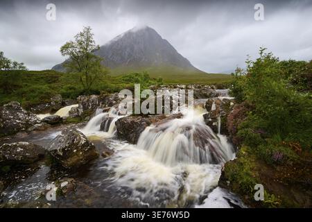 Ruhige Wasserlandschaft mit stilvollen Wasserfällen und einem imposanten, wolkenbedeckten Berg im Hintergrund, Buachaille Etive Mor Aussichtspunkt, River Coupal Stockfoto