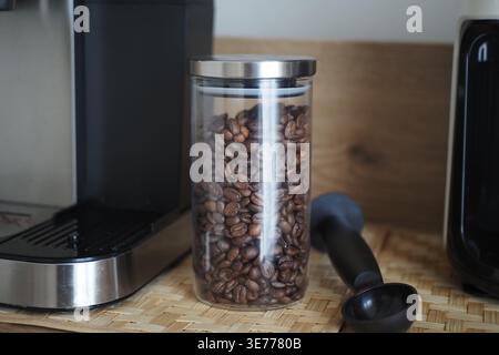 Kaffeebohnen in einem Glas neben einer Kaffeemaschine auf der Theke Stockfoto