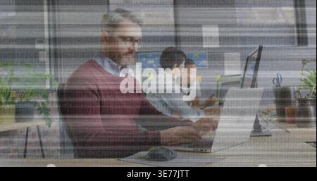 Arbeitender reifer Mann in burgunderrotem Pullover, der auf silbernem Laptop am gemeinsamen Holztisch schreibt, Kopierraum Stockfoto