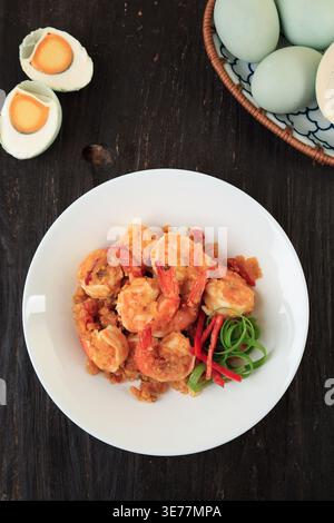 Top View Salted Egg Braten Shrimps mit Curryblättern serviert auf weißer Platte. Udang Telur ASIN auf Holztisch Stockfoto