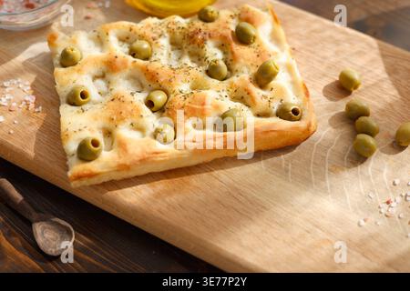 Nahaufnahme traditioneller italienischer Olive-Focaccia auf Holzbrett mit Kopierraum. Der Hochwinkel hebt knusprige, goldkrustgrüne Oliven hervor, die getrocknet sind Stockfoto