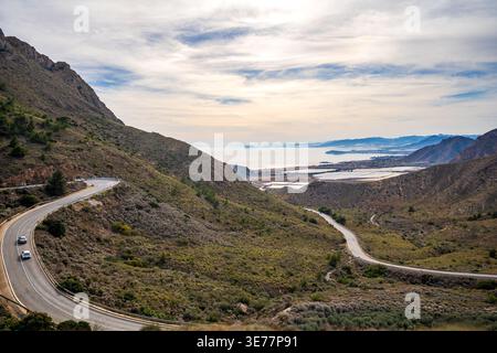 Eine gewundene Straße schlängelt sich durch die trockenen Berge der Sierra de la Muela in Richtung Meer. Die aussicht fängt die wilde Schönheit der Costa Calida in der Nähe von Cartagena ein, Stockfoto