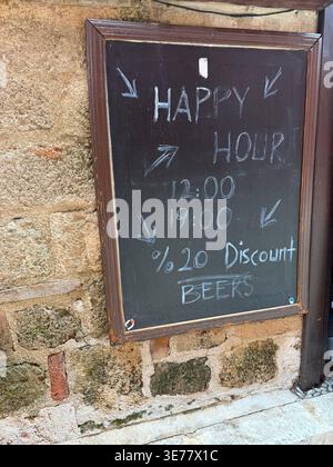 Tafelschild mit Happy Hour-Zeiten und Bierrabatt draußen auf rustikaler Steinmauer. Mobiles Foto Stockfoto