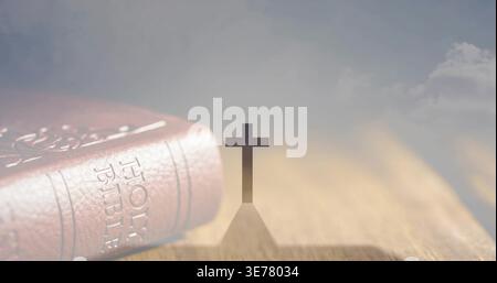 Schlichte Kreuzsilhouette, die langen Schatten auf hölzernen Tischplatten erzeugt, mit der Heiligen Bibel aus Leder Stockfoto