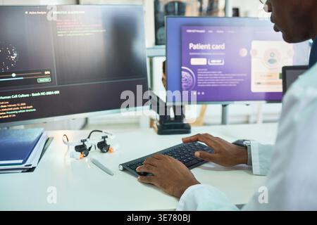 Afroamerikanischer männlicher Arzt, der am Arbeitsplatz schreibt, die Schnittstelle für Patientenkarten und medizinische Analysedaten überprüft. Unterstützung von Gesundheitssoftware, digitalen Aufzeichnungen, Telemedizin-Marketing Stockfoto