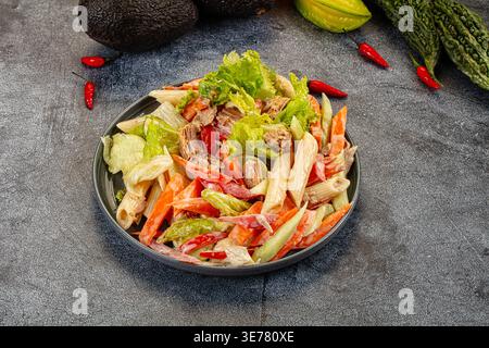 Appetitlicher Nudelsalat mit Thunfisch und Gemüse in einer cremigen Sauce. Die Top-Down-Ansicht auf dunklem Hintergrund hebt frische rote, grüne und beige Farben hervor. P Stockfoto