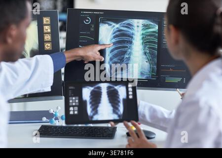 Ärzte, die Röntgenaufnahmen des Thorax auf Monitor und Tablet überprüfen, zeigen auf Lungenanalysen zur Diagnose und Zusammenarbeit. Ideal für das Marketing in den Bereichen Gesundheitstechnologie, Radiologie und KI-Diagnostik Stockfoto