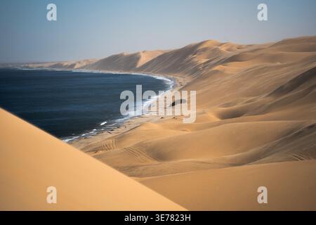 Der Blick auf die sanften goldenen Sanddünen trifft auf das tiefblaue Meer unter einem klaren Himmel, was einen beeindruckenden Kontrast in Anichab, Erongo, Namibia, schafft. Stockfoto