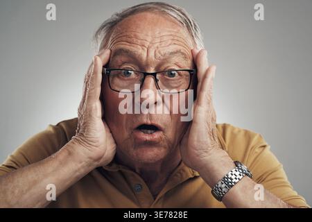 Porträt, schockiert und alter Mann im Studio, Brille und Ansage auf grauem Hintergrund. Brillen, omg oder ältere Menschen mit Gesichtsausdruck, Reaktion Stockfoto