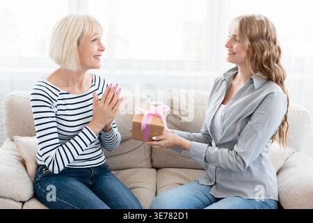 Eine junge Frau gratuliert ihrer älteren Mutter mit einer Geschenkbox Stockfoto
