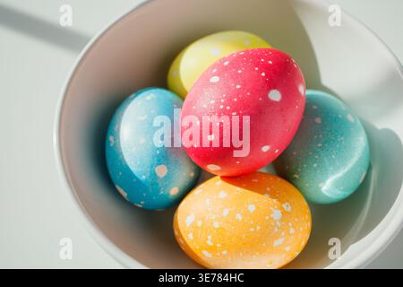 Natürliche Hühnereier in verschiedenen hellen Farben und weißen Punkten in der Schüssel auf weißem Tisch unter der Morgensonne. Kreative Ostertraditionen, homem Stockfoto