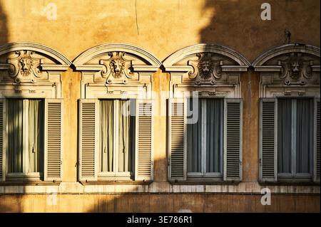 Warmes Licht an Fensterläden oder italienisches Holz-Jalousie, gezogene Vorhänge, die auf verborgene Geschichten und ungesehene Leben im Inneren hinweisen, wecken Privatsphäre und Ruhe Stockfoto
