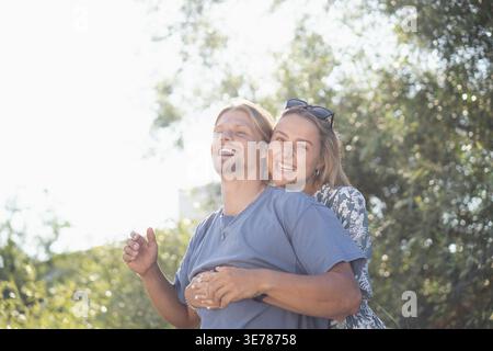Sorgloses Paar genießt einen fröhlichen Huckepack-Ritt in sonniger Natur Stockfoto