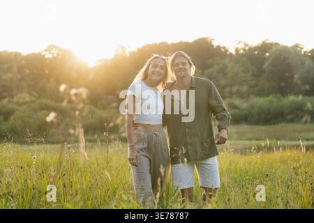 Glückliches Paar, das nahe beisammen in der leuchtenden Landschaft des Sonnenuntergangs steht Stockfoto