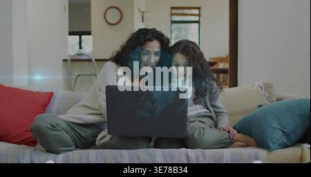 Mutter und Kind in legeren Kleidern sitzen auf einem gestreiften Sofa und teilen sich einen Laptop mit roten, blaugrünen Kissen Stockfoto