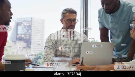 Führender Mann mit Brille, kariertes Hemd, das auf dem Laptop im Besprechungsraum präsentiert, mit Datenüberlagerungen Stockfoto