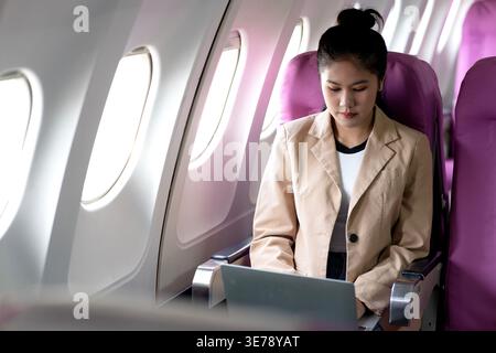 Junge Geschäftsfrau benutzt Laptop, während sie Flugzeuge für Arbeit und geschäftliche und persönliche Kommunikation fliegt Stockfoto