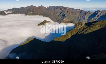 Der Blick auf den Mittelgebirge von Madeira zeigt Gebirgszüge über niedrigen Wolken in der Nähe von Pico do Arieiro und Pico Ruivo, lange Schatten an bewaldeten Hängen und Stockfoto