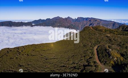 Aus der Vogelperspektive auf Madeira, Kamm zwischen Pico do Arieiro und Pico Ruivo, Wolken Pool in Tälern, gewundener Schotterweg über Strauchhügel, Mittagslicht, tiefe s Stockfoto