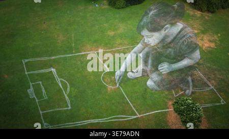 Luftaufnahme eines riesigen Mädchenbildes, das ein Fußballfeld auf dem hellgrünen Gras zeichnet, ein skurriler Kontrast von Skala und Kunstfertigkeit, Genève, SW Stockfoto