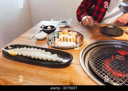 Koreanischer Grilltisch mit Grill und Beilagen zum Kochen von Fleisch, geselliges Abendessen, asiatische Küche Stockfoto