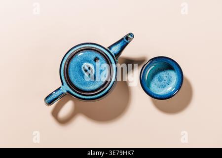 Minimaler Blick von oben mit blauer Keramik-Teekanne und Tasse auf beigefarbenem Hintergrund, sauberes asiatisches Teekonzept Stockfoto