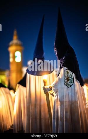 Nazarener aus der Bruderschaft La Estrella beleuchten die Carmen-Kapelle neben der Triana-Brücke während der Palmensonntagsprozession in der Nacht in Sevilla, S. Stockfoto