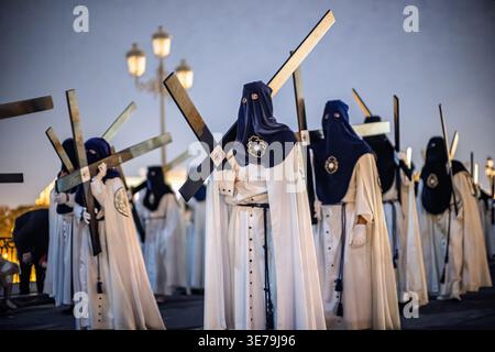 Narazenos de la Estrella-Mitglieder tragen hölzerne Kreuze als Buße während der Palmsonntagabend-Prozession der Karwoche in Sevilla, Andalusien, Spanien. Stockfoto