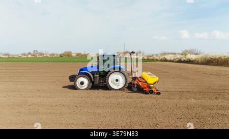 Aus der Vogelperspektive eines blauen Traktors, der den Boden auf einem weiten Feld unter hellem Himmel bearbeitet, Sremska Mitrovica, Vojvodina, Serbien. Stockfoto