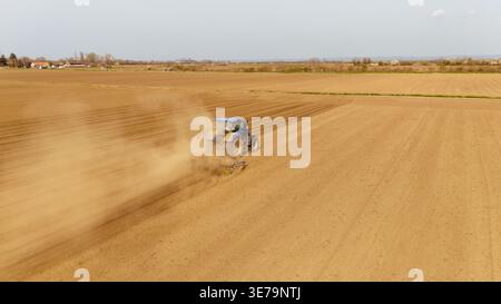 Aus der Vogelperspektive eines blauen Traktors, der die trockene, braune Erde bearbeitet, Staub unter einem hellen Himmel aufwirbelt, Sremska Mitrovica, Vojvodina, Serbien. Stockfoto