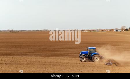 Aus der Vogelperspektive eines blauen Traktors, der Staub aufwirbelt, während er die riesigen braunen Felder unter hellem Himmel befüllt, Sremska Mitrovica, Vojvodina, Serbien. Stockfoto