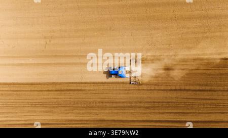 Aus der Vogelperspektive eines blauen Traktors, der durch das weite, trockene Land schneidet und Staub aufwirbelt, Sremska Mitrovica, Vojvodina, Serbien. Stockfoto