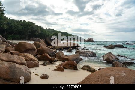Tropische Küste mit großen Felsen, türkisfarbenem Meer, Sandstrand, Baumästen und fernen Inseln unter hellem Himmel, ideal für Reisen, Urlaub, Natur und Stockfoto