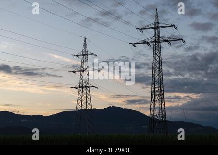 Stromübertragungstürme stehen in einer natürlichen Umgebung, wenn die Sonne untergeht, hoch und verbinden Stromleitungen mit dem Netz und der Landschaft. Stockfoto