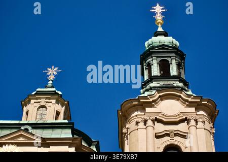 Barocke Kirchtürme mit goldenen Kreuzen erheben sich vor einem leuchtend blauen Himmel mit verzierten Steinmetzwerken, patinierten Kupferkuppeln und einem historischen Bogen Stockfoto