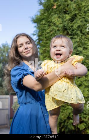 Die Frau hebt ihre kleine Tochter hoch in den Armen, spielt glücklich mit ihr und genießt den Moment in der Natur im Park. Das Baby und die Mutter haben ein Bein Stockfoto