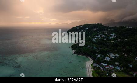 Wunderschöner Sonnenuntergang mit Orangentönen über mehreren Inseln und ruhigem Meereswasser, mit Silhouetten von Hügeln. Seychellen, Mahe. Stockfoto