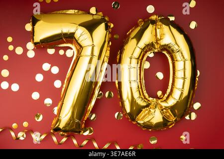 Herzlichen Glückwunsch zum Geburtstag. 70 Jahre alt. Goldballons Nummer 70 auf rotem Hintergrund mit Konfetti, siebzigjähriges Jubiläum. Stockfoto