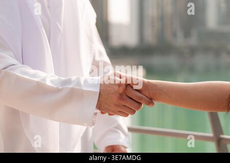 Eine Asiatin und ein Emirati treffen sich in Dubai Marina, um über Immobilieninvestitionen zu diskutieren und einen Deal mit einem Handschlag abzuschließen. Stockfoto